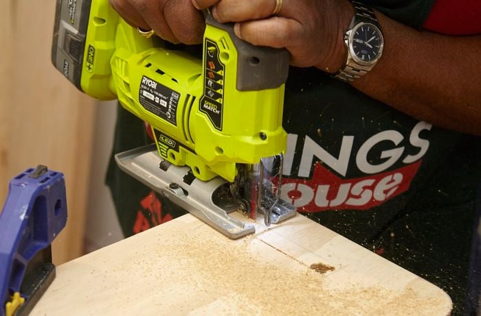 Person using jigsaw to cut out small rectangular shape on piece of ply wood.