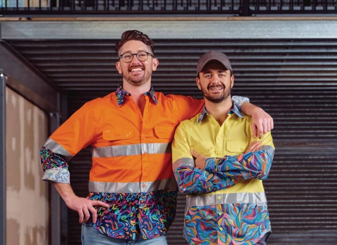 TIACS co-founder Ed Ross stands smiling and pointing to the slogan on the back of Dan Ross brightly coloured shirt