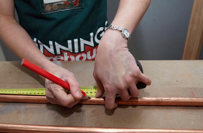Person measuring and marking copper pipe with tape measure and pencil