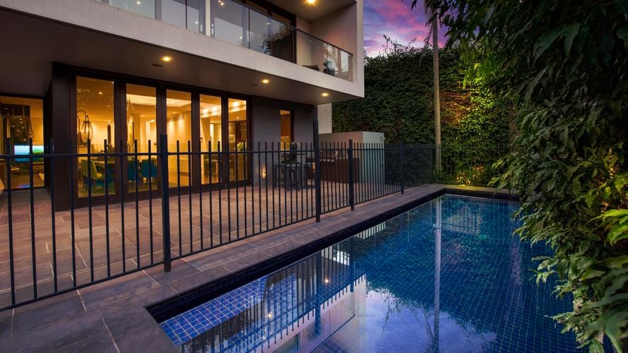 A pool outside a modern two storey house with a purple night sky.