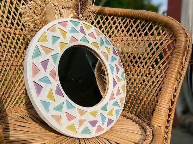 Mirror mosaiced with pastel coloured glass leaning on a wicker chair. 