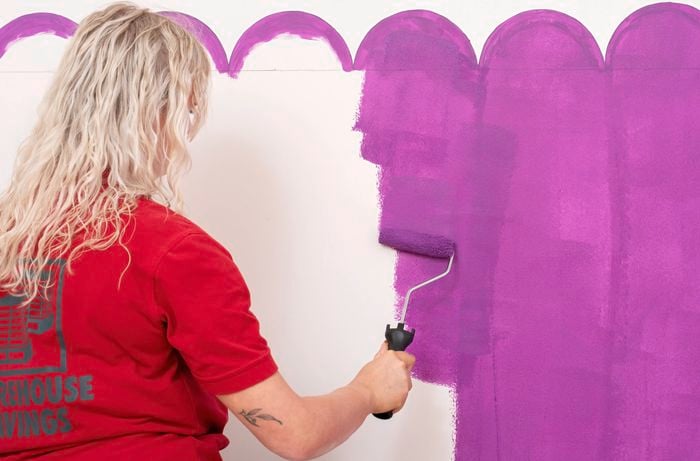 A Bunnings team member is using a paint roller to fill in the centre of each scallop with purple paint.