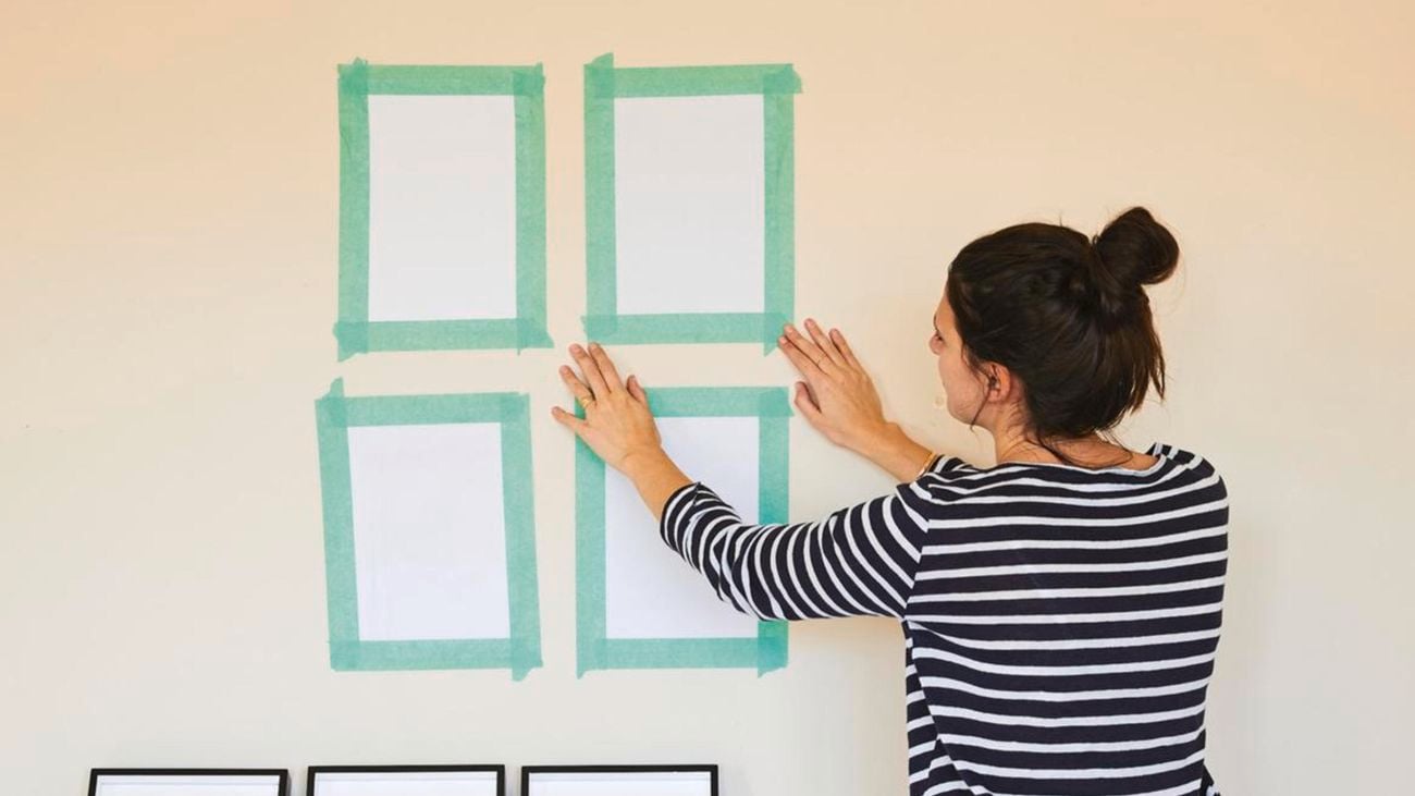 A woman using tape to plan where she will hang the frames.