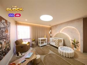 Neutral baby bedroom with brown and tan colours. Showcasing a cot and change table in front of an arched feature wall with feature lighting. There is a large chair in the corner and a play area on an arched pattern rug.