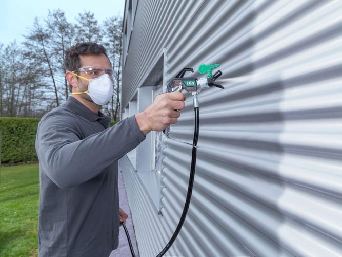 Wagner Control Pro Hybrid Gun with HEA tip spraying outdoor corrugated metal with light grey paint.