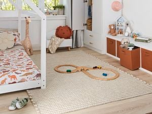 Kids bedroom with white toddler bed and cupboard, printed ceiling light shade and horizontal storage cabinet with brown drawers and white walls