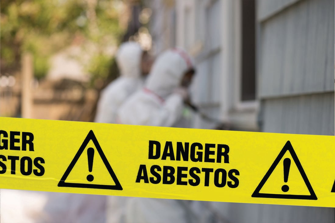Yellow hazard tape in front of two hazmat workers with the words Danger Asbestos