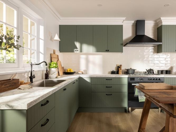 Green modern kitchen with a white marble benchtop, black sink mixer and a wooden table in it.