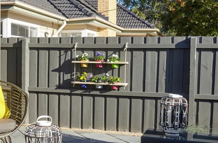 A pot plant holder with six pots hanging on a paling fence