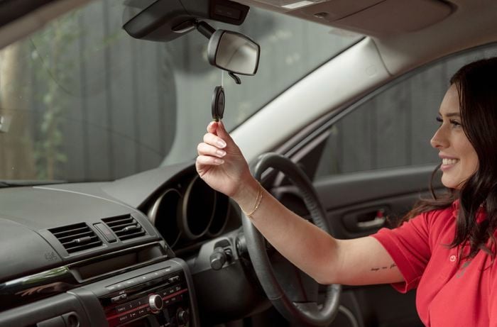A Bunnings team member sitting on a car seat with a smile, holding a hanging air freshener.