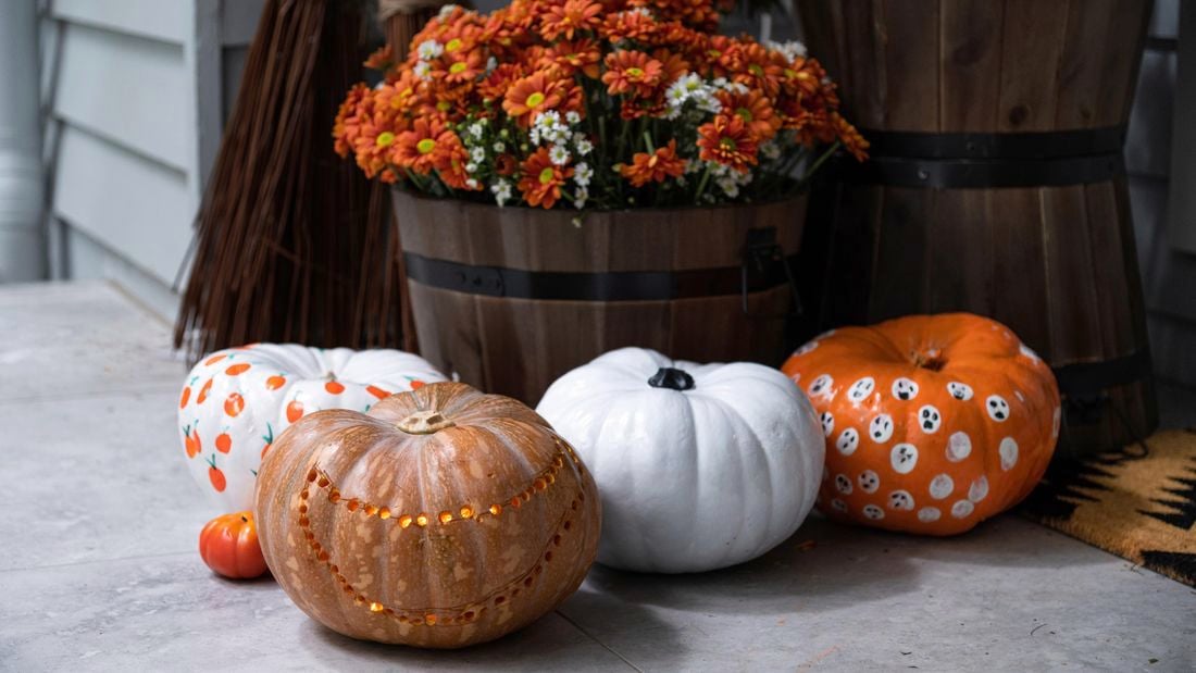 Close up of three decorated pumpkins in front of a potted plant in a barrel.