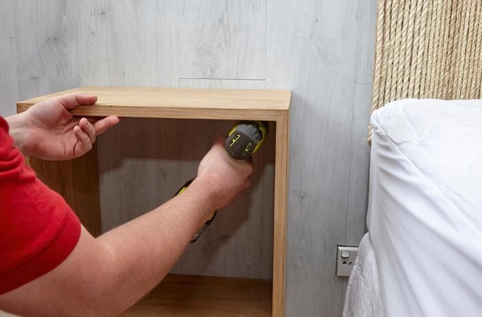 Person attaching shadow box frame to wall with a drill.