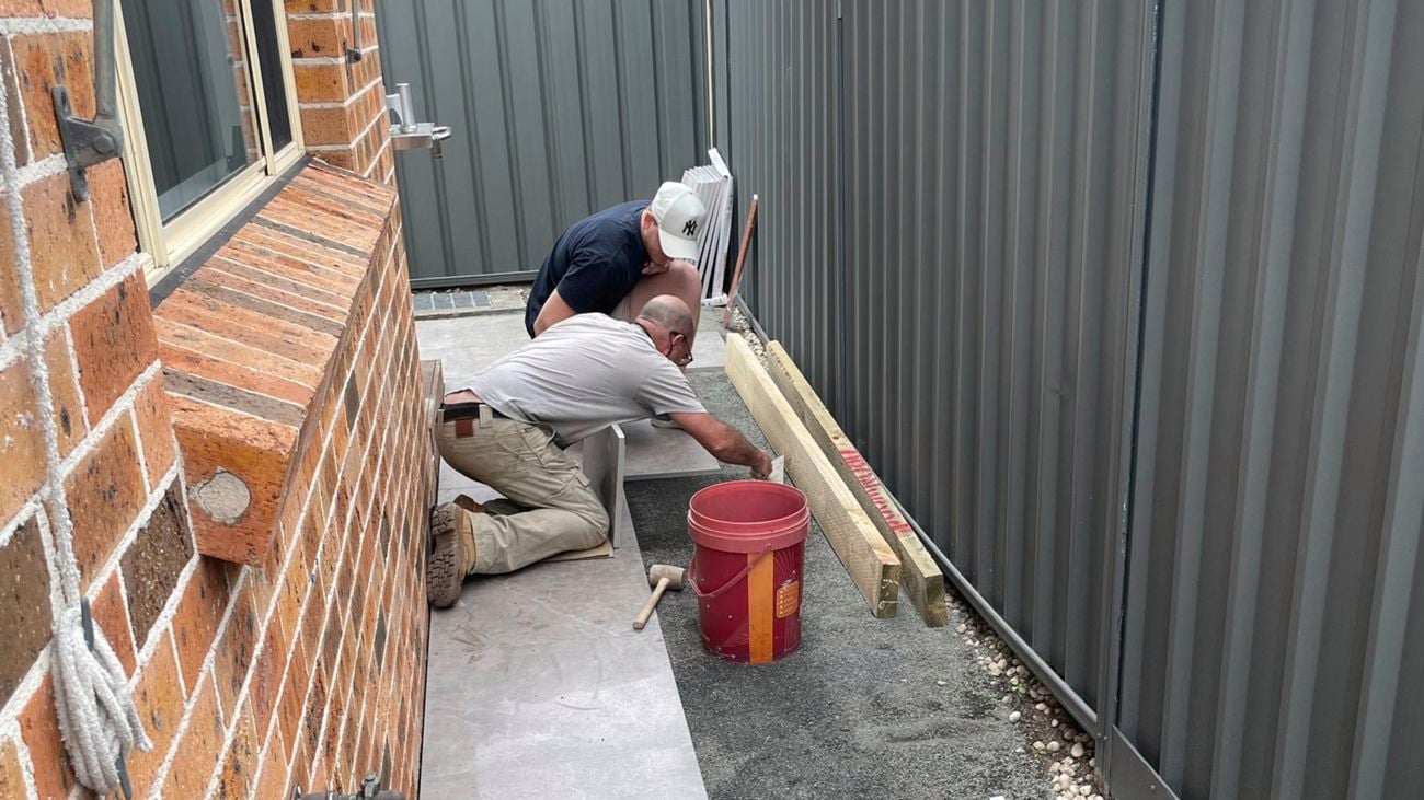 side of house with two men laying some pavers