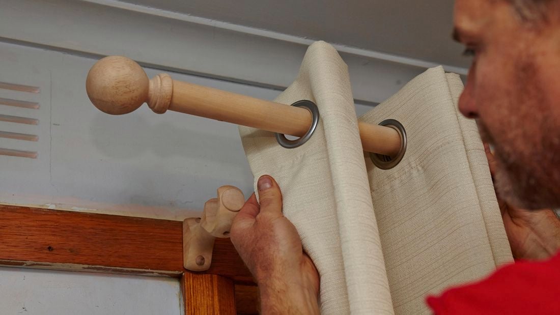 Person fitting curtains to curtain rod.