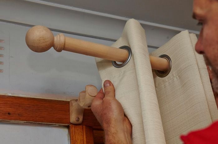 Person fitting curtains to curtain rod.