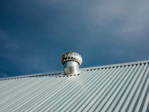 Close up shot of a roof vent on a tin roof with a deep blue sky in the background