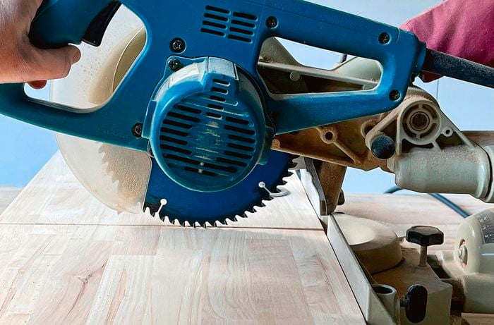 A person holding a circular saw against a piece of timber