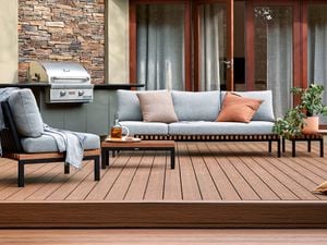A Barbecue and outdoor setting on a timber decking with a cushion and pot plants on it.