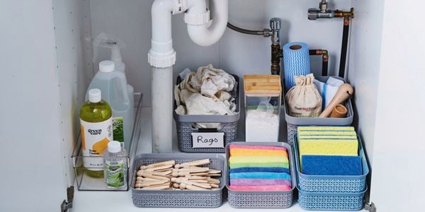 Close up of a vanity cabinet with doors opened showing organised cleaning products and sponges in basket organisers.