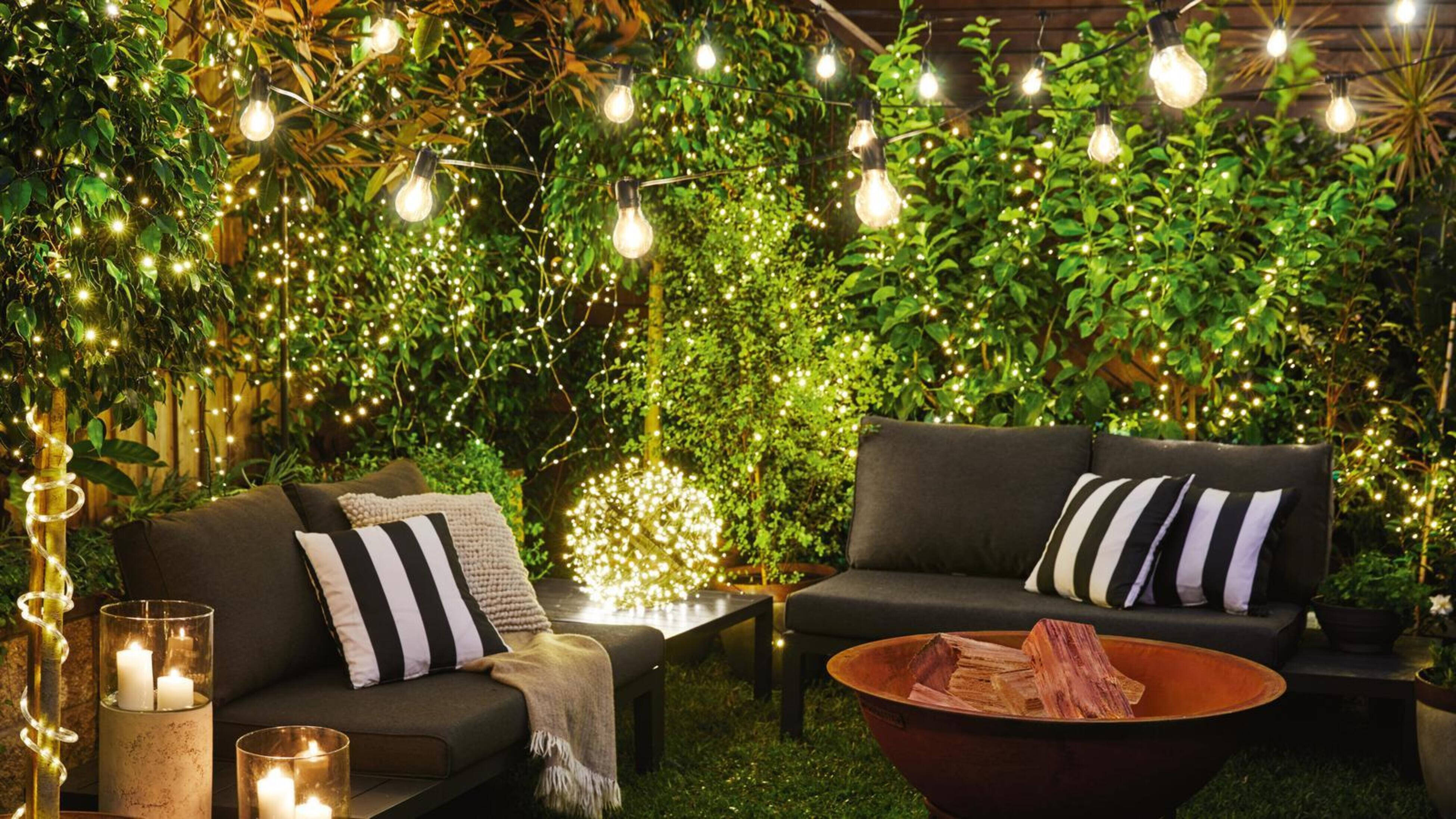 Outdoor area with lights hanging in the trees and an outdoor setting in it.