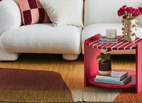 A red and white striped two tier coffee table with a vase, candle and book on top next to a white lounge
