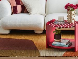A red and white striped two tier coffee table with a vase, candle and book on top next to a white lounge
