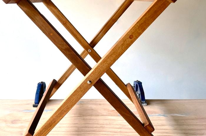 The frame of a foldable chair propped upright, attached with clamps to a wooden table.