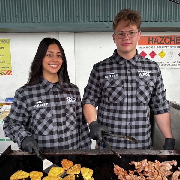 Bunnings Trade team members wearing Movember flannel shirts cooking bacon and hash browns on a barbecue for Movember 