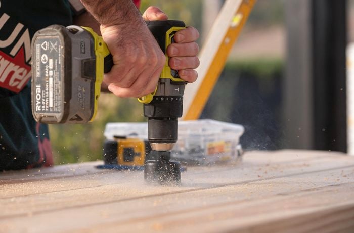 Using a power tool to cut an umbrella hole in the picnic table