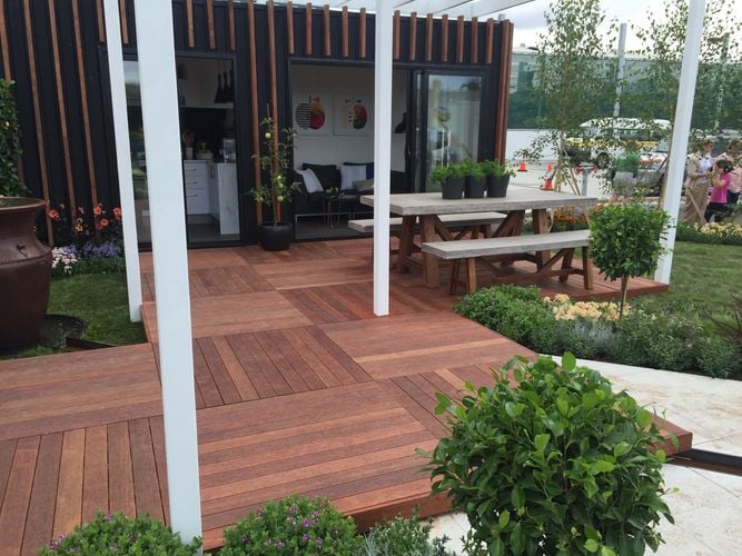 A crosshatched deck with park bench on the edge of a flowerbed and lawn