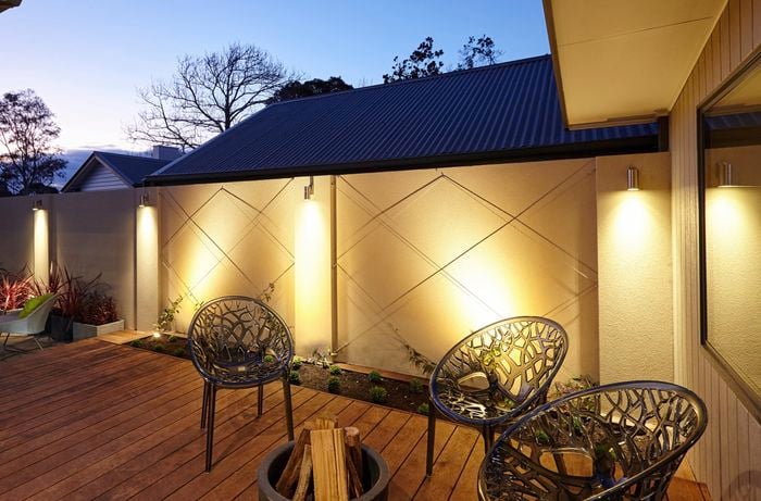 A deck area at night with a fire drum and downlights on the walls