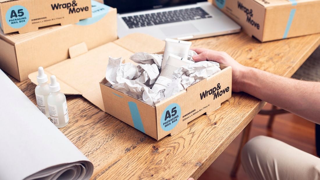 A person packs skincare products in a small Wrap & Move box filled with Wrap & Move’s kraft paper