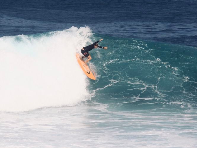 Surfer dropping down the face of a large wave on an orange Summer vibes board.
