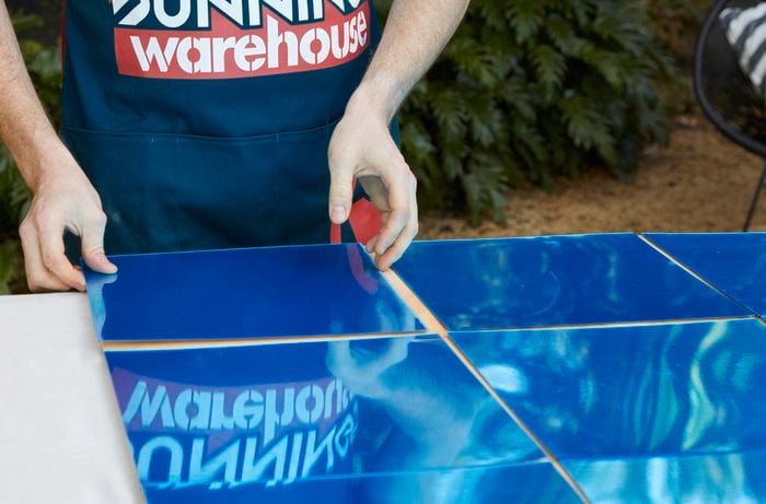 Person aligning acrylic mirror squares on plywood.