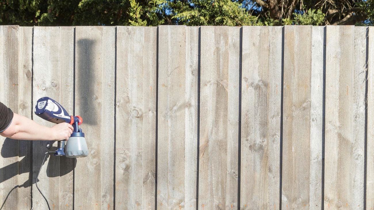 Person spray painting a wooden fence.