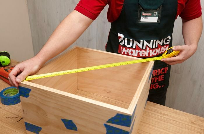 Person measuring DIY shadow box frame corner-to-corner with measuring tape.