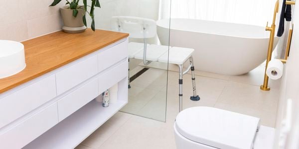 Bathroom with white bathroon cabinet with timber top, toilet, free standing bath and assited bench