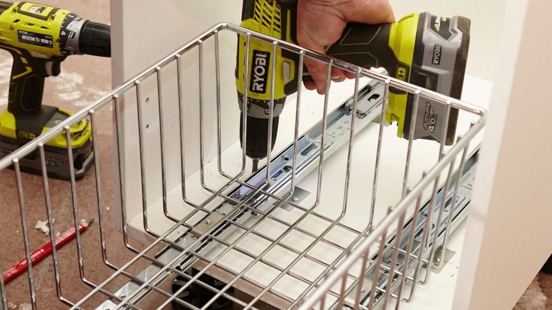 A person installing runners for a wire basket in a cabinet