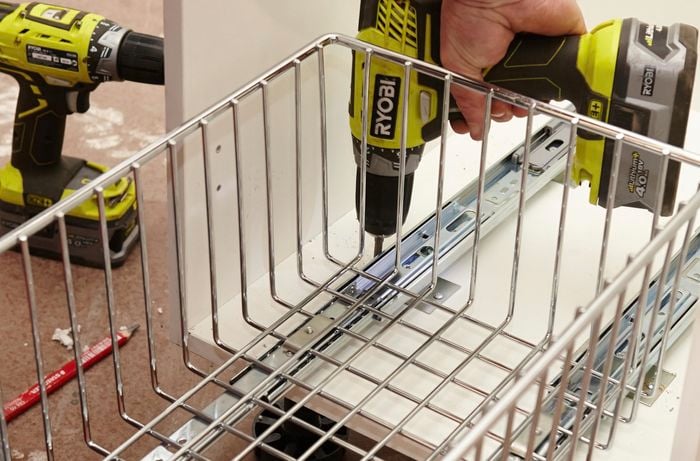 A person installing runners for a wire basket in a cabinet