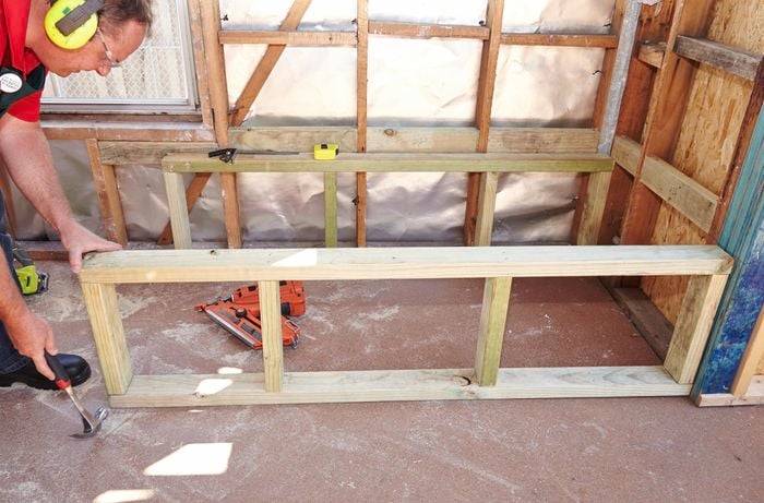 A person using a hammer to adjust the position of a timber bath frame 