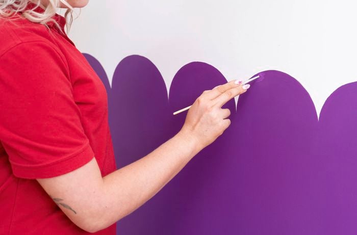 A person is using a small brush to refine and touch up the curved edges of a scalloped wall. 