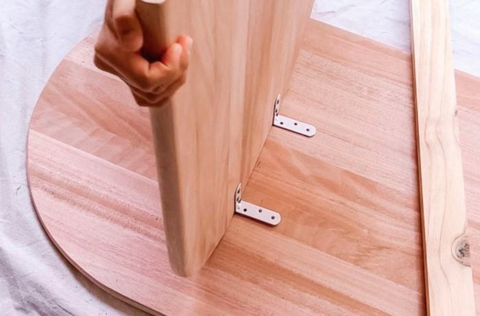 Person attaching table legs to table top with through brackets.