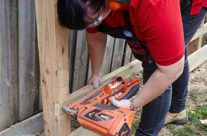 A person wearing protective gear attaching a rail to a fence post using a nail gun
