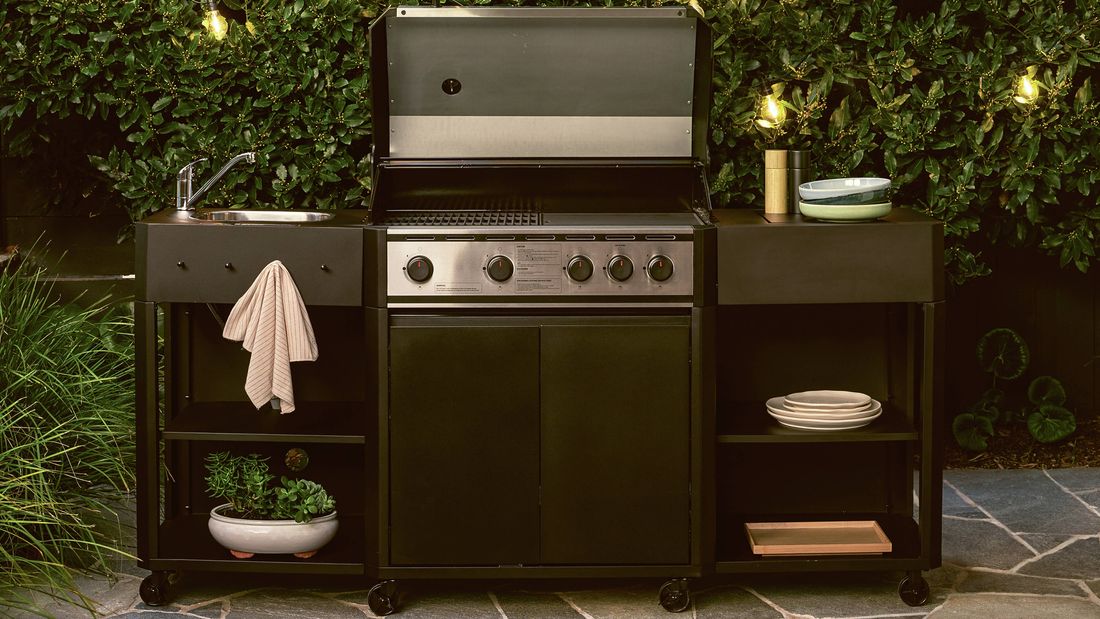utdoor barbecue kitchen with BBQ, sink, and shelving against a green hedge with string lights