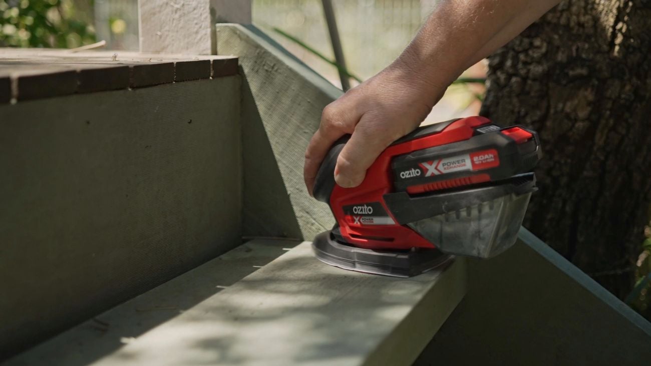 A hand using a detail sander to sand paint from outdoor timber step outside