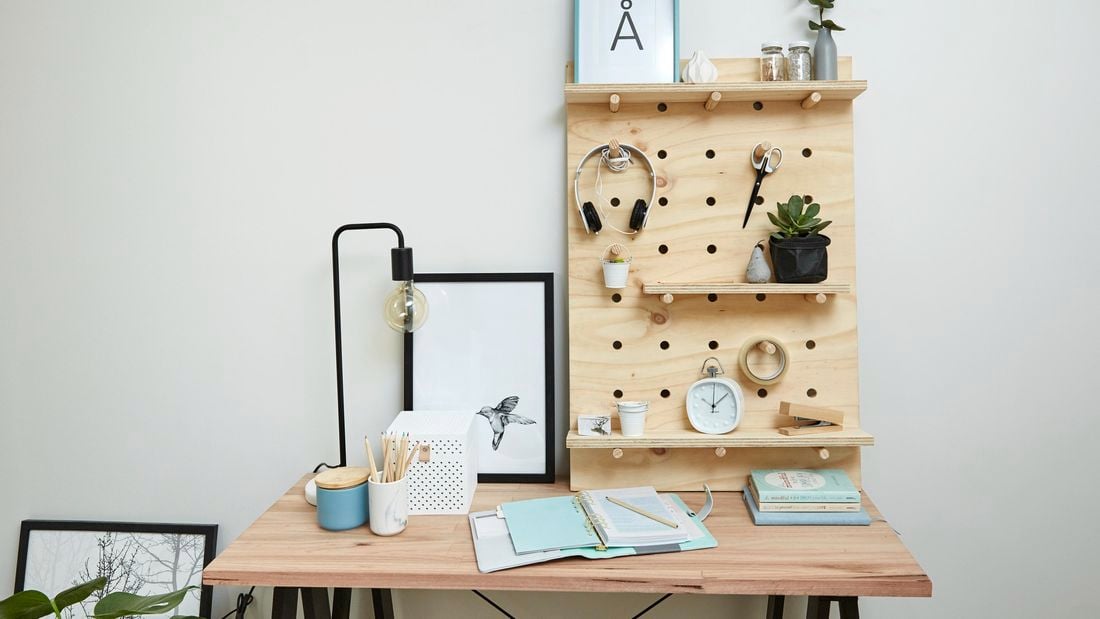 A pegboard shelf of plywood and dowel holding headphones and other objects