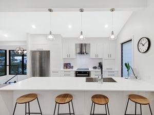 Shot of white kitchen with black accents and four stools in-front of benchtop.