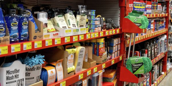 Retail shelving displaying car care and cleaning products, including wash mitts, microfibre cloths, sponges, polishes and automotive fluids.