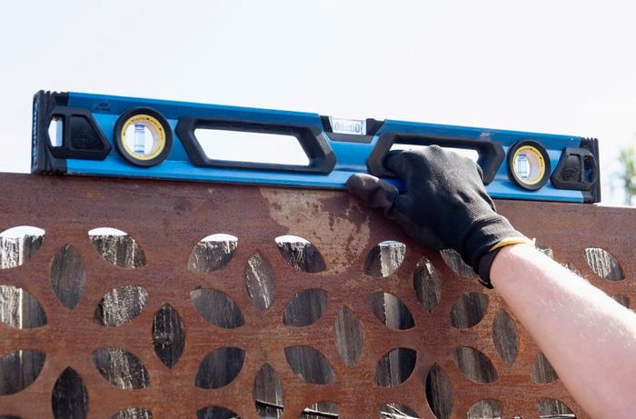 A person holding a spirit level on the top of a steel screen