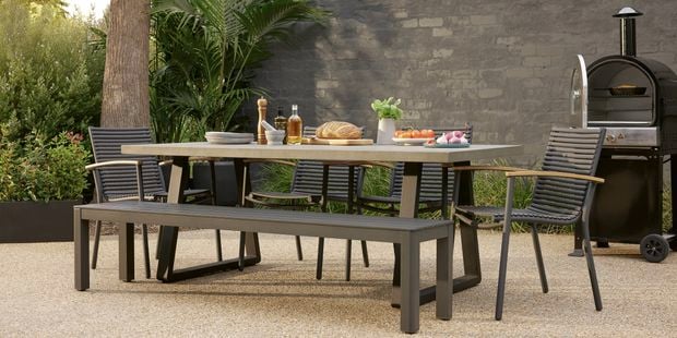 Black outdoor setting and BBQ sitting on timber decking with potted plants